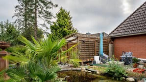 Ein Garten mit Teich, Holzelementen und Kübelpflanzen.