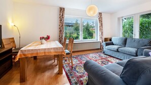 Ein Wohnzimmer mit Esstisch, Sofa und großen Fenstern.