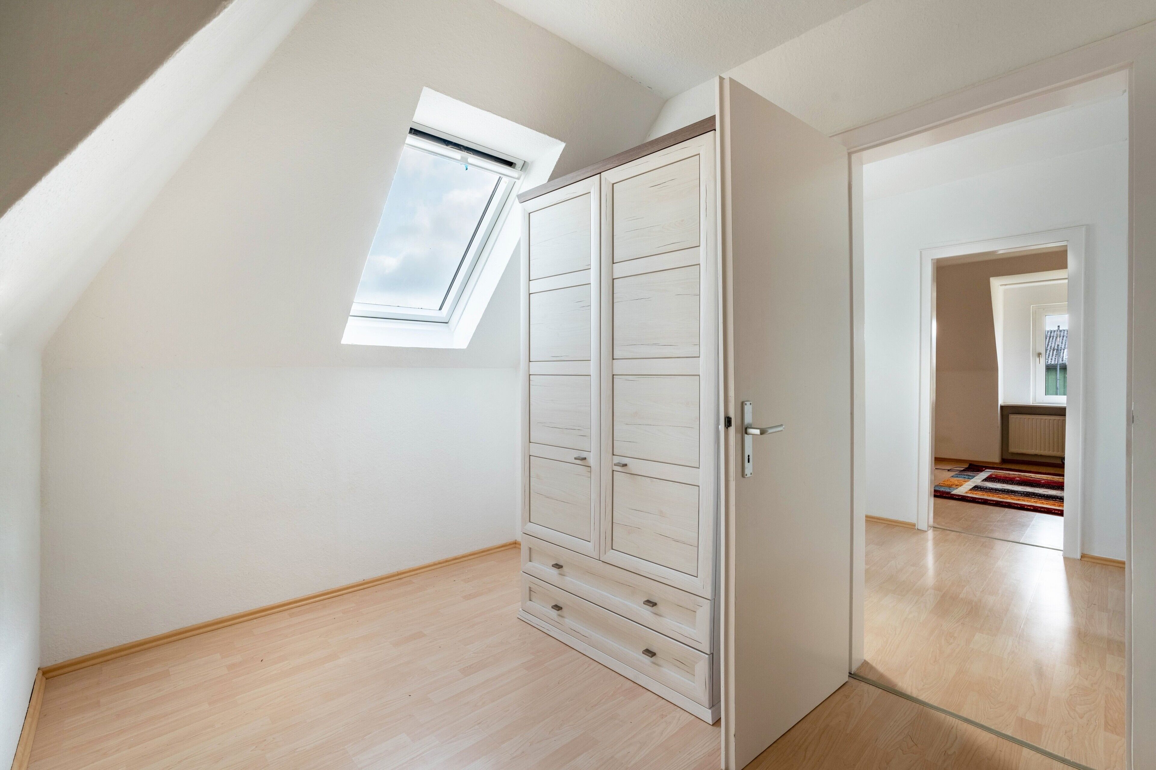 Une pièce vide avec une lucarne, un plancher en bois et une armoire.