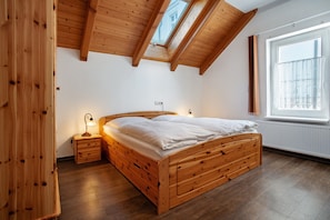 A wooden bed in a room with a sloped ceiling and a window.