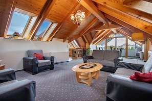 A spacious loft-style room with high ceilings, wooden beams, and large windows.