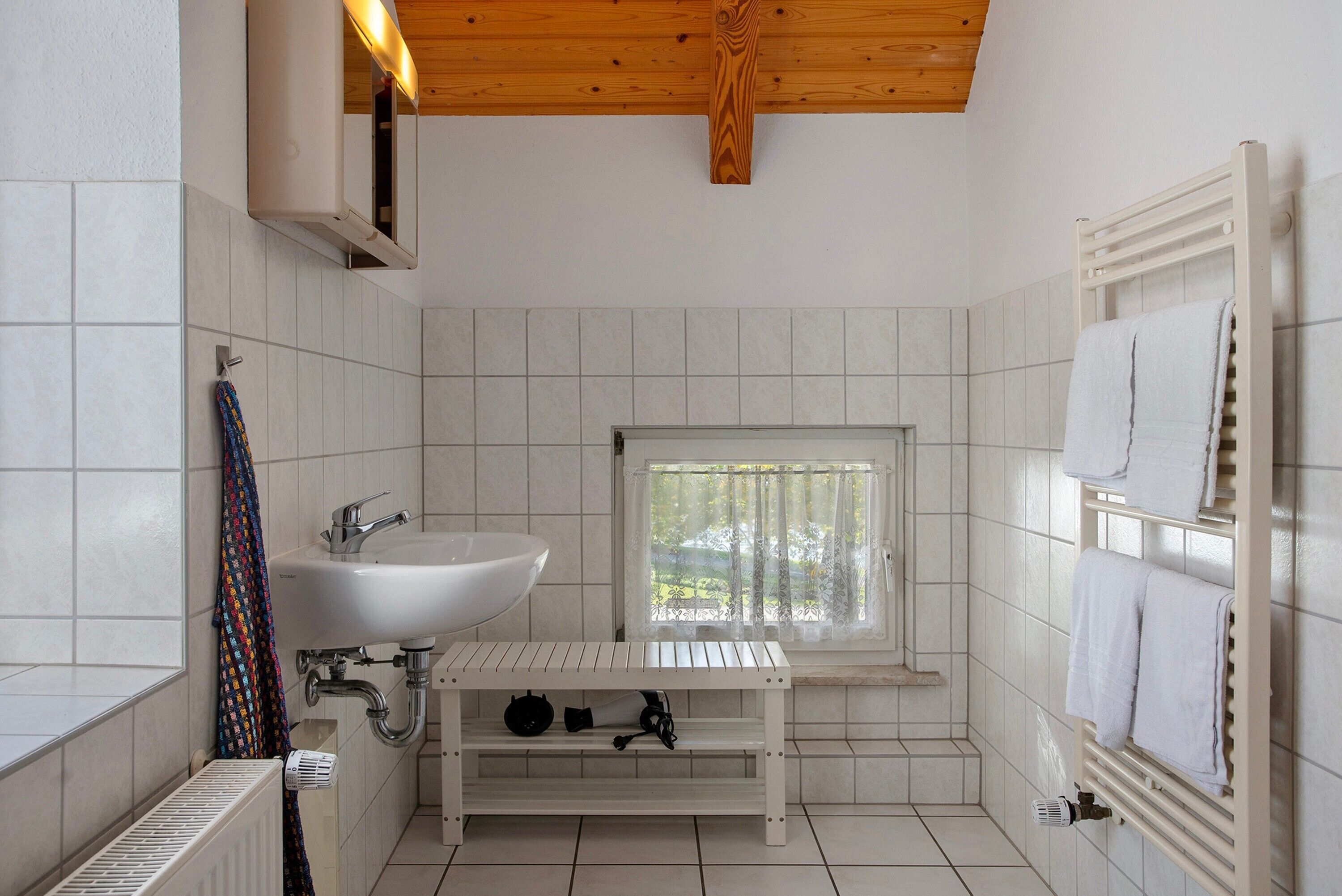 A bathroom with a white sink, a window, a towel rack, and a radiator.