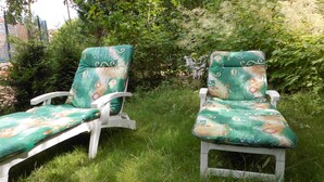 Two white lounge chairs with green patterned cushions in a grassy outdoor area.