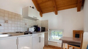 Une cuisine avec des meubles blancs, un four à micro-ondes, une machine à café et une fenêtre donnant sur les arbres.