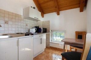 Cozinha com armários brancos, micro-ondas, cafeteira e janela com vista para árvores.