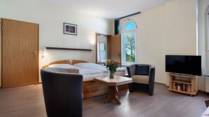 A bedroom with a bed, a TV, a small table with a vase, and a chair.