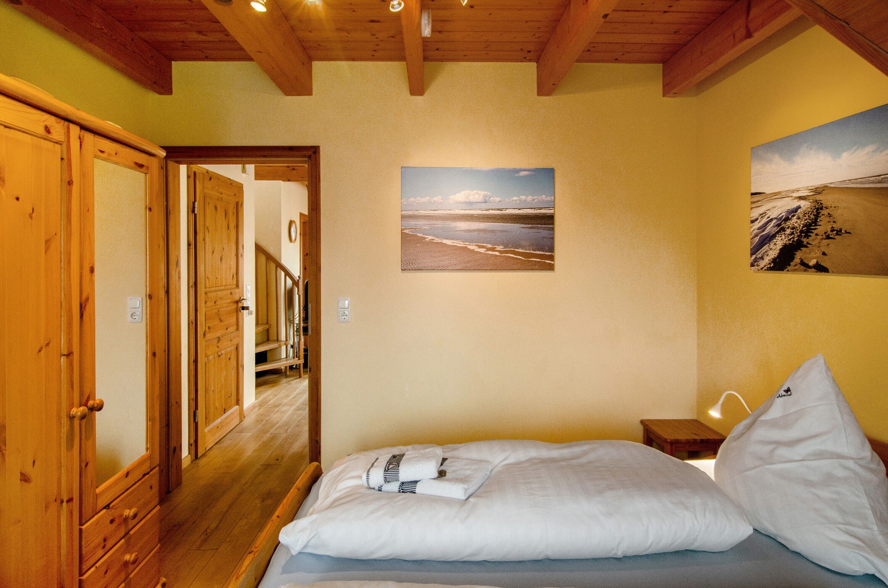 A bedroom with a bed, wooden wardrobe, and a painting of a beach scene.