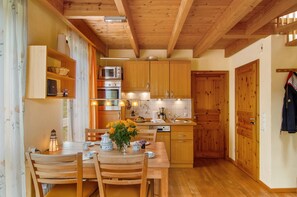 A wooden interior with a dining table, chairs, a kitchen area with wooden cabinets, a microwave, and a sink.