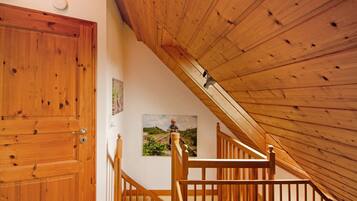 Eine Holztreppe führt zu einem Dachboden mit geneigter Decke, einer Holztür und einem gerahmten Bild an der Wand.