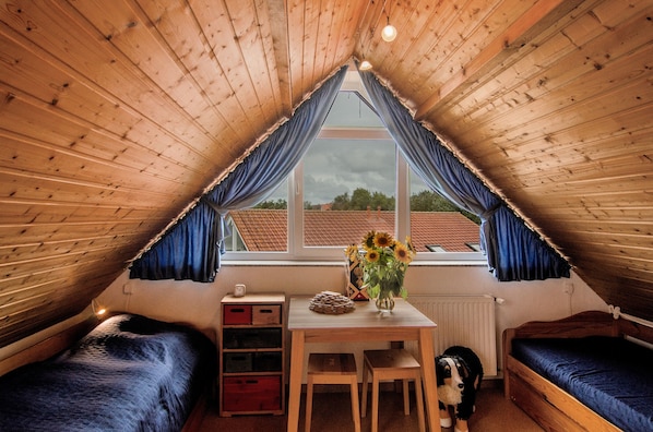 A cozy attic room with a sloped ceiling, a wooden table with a vase of flowers, a dog, and two beds.