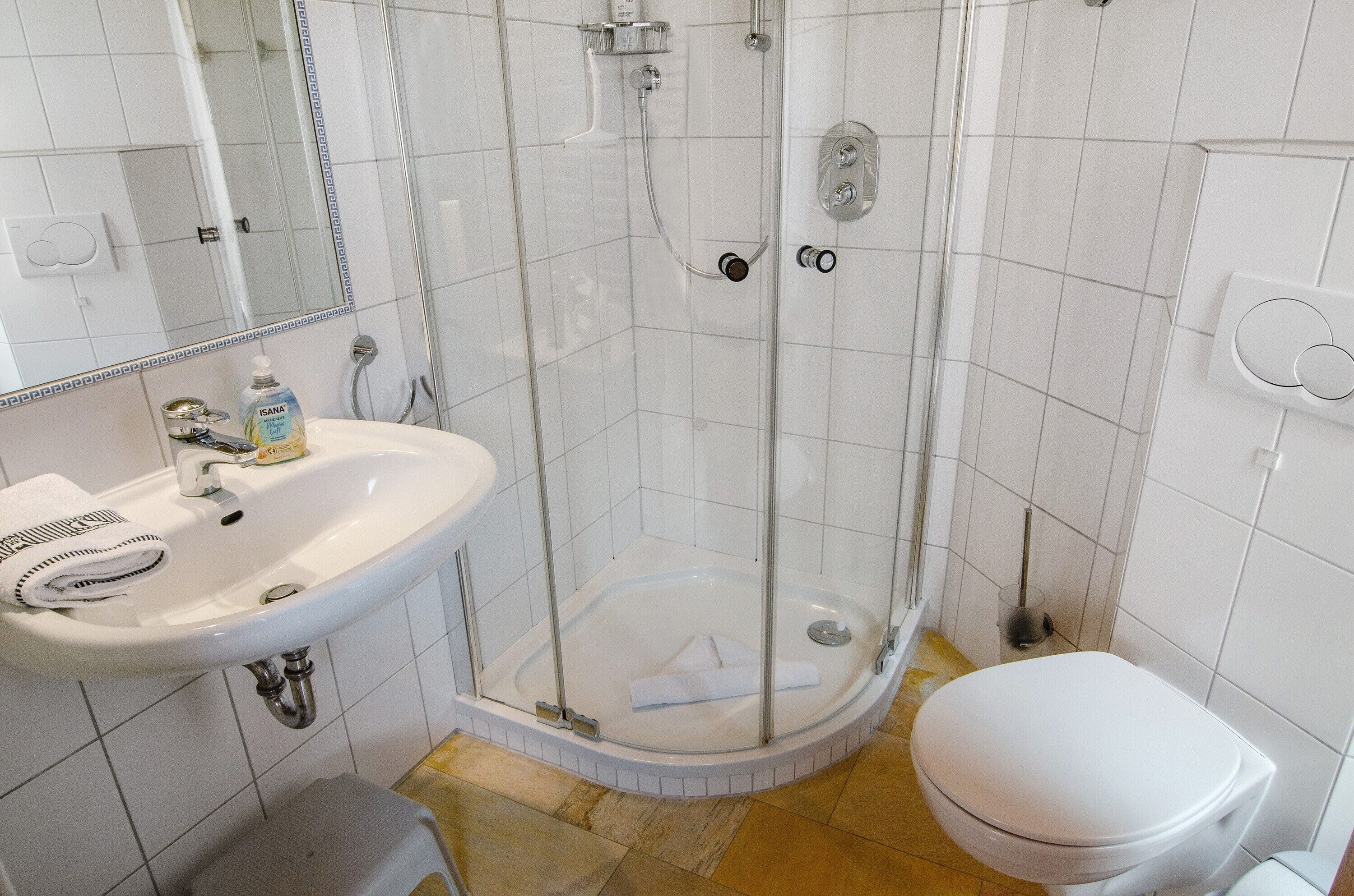 A bathroom with a glass-enclosed shower, a sink with a soap dispenser, and a toilet.