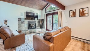 A cozy living room with a fireplace, leather sofas, and a stone wall.