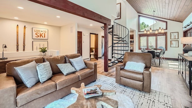 A spacious living area with a brown leather sofa, a brown armchair, and a wooden coffee table. A spiral staircase leads to an upper level.