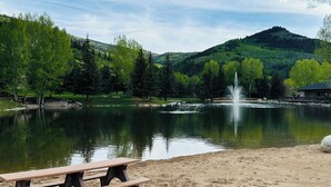 A lakeside view with a picnic table, calm water, and a fountain.