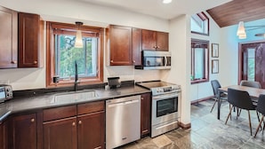 A modern kitchen with wooden cabinets, stainless steel appliances, a dishwasher, and a dining area with a table and chairs.