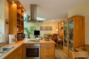 A kitchen with wooden cabinets, a stove, a microwave, and a large window. - Holiday Home 'Haus Admiral  Wintergarten' with Private Terrace, Private Garden and Wi-Fi (Spiekeroog)