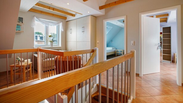 A spacious room with a wooden staircase, a window with curtains, and a view of the outside.