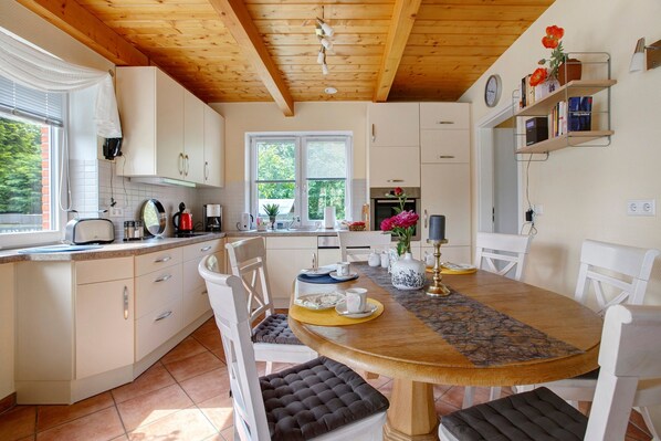 Una cocina con armarios blancos, techo de madera y una mesa de comedor con sillas.