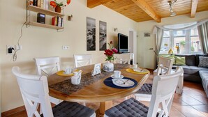A dining area with a wooden table, white chairs, and a bookshelf with books and flowers.