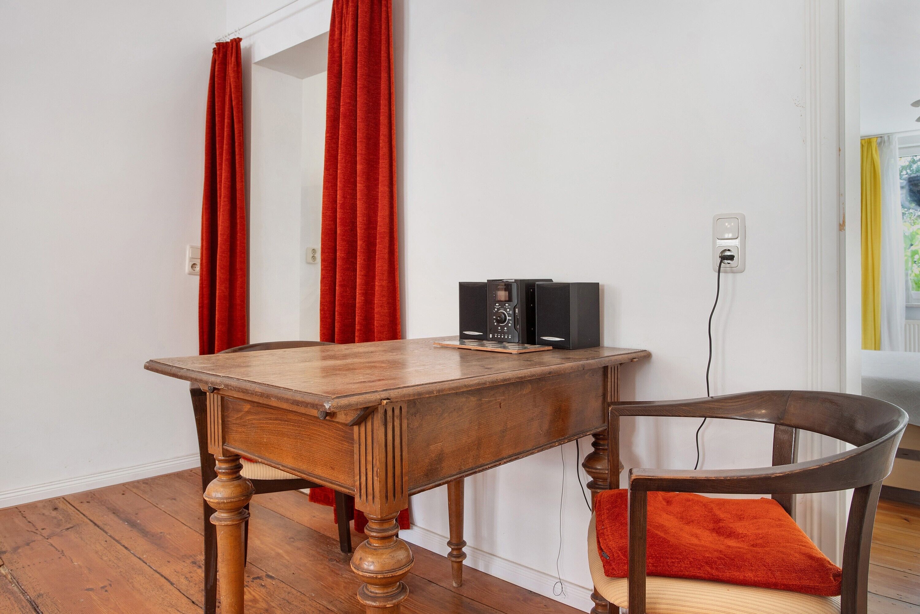 A wooden table with a speaker, a chair with a cushion, and a red curtain.