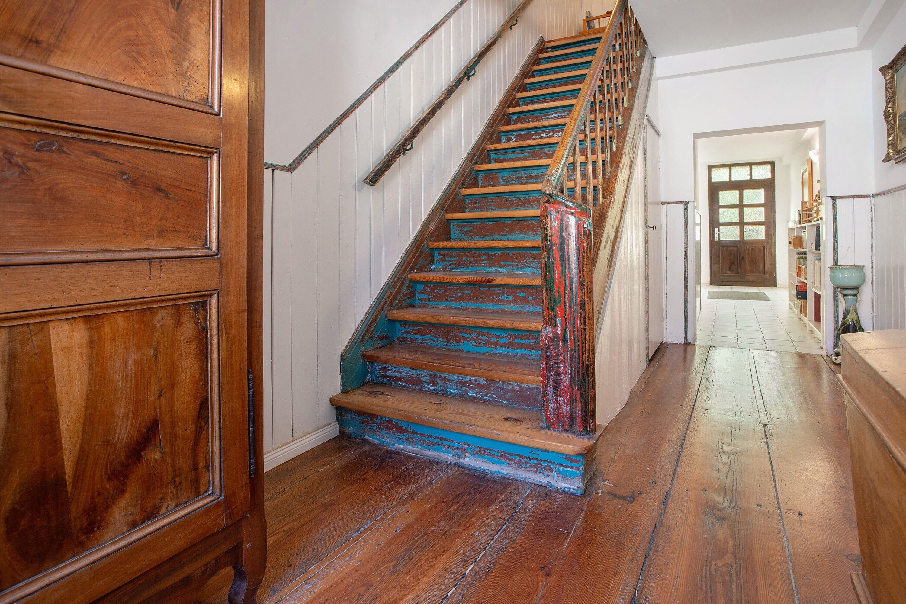 Un escalier en bois peint en bleu, des murs blancs et une porte en bois.