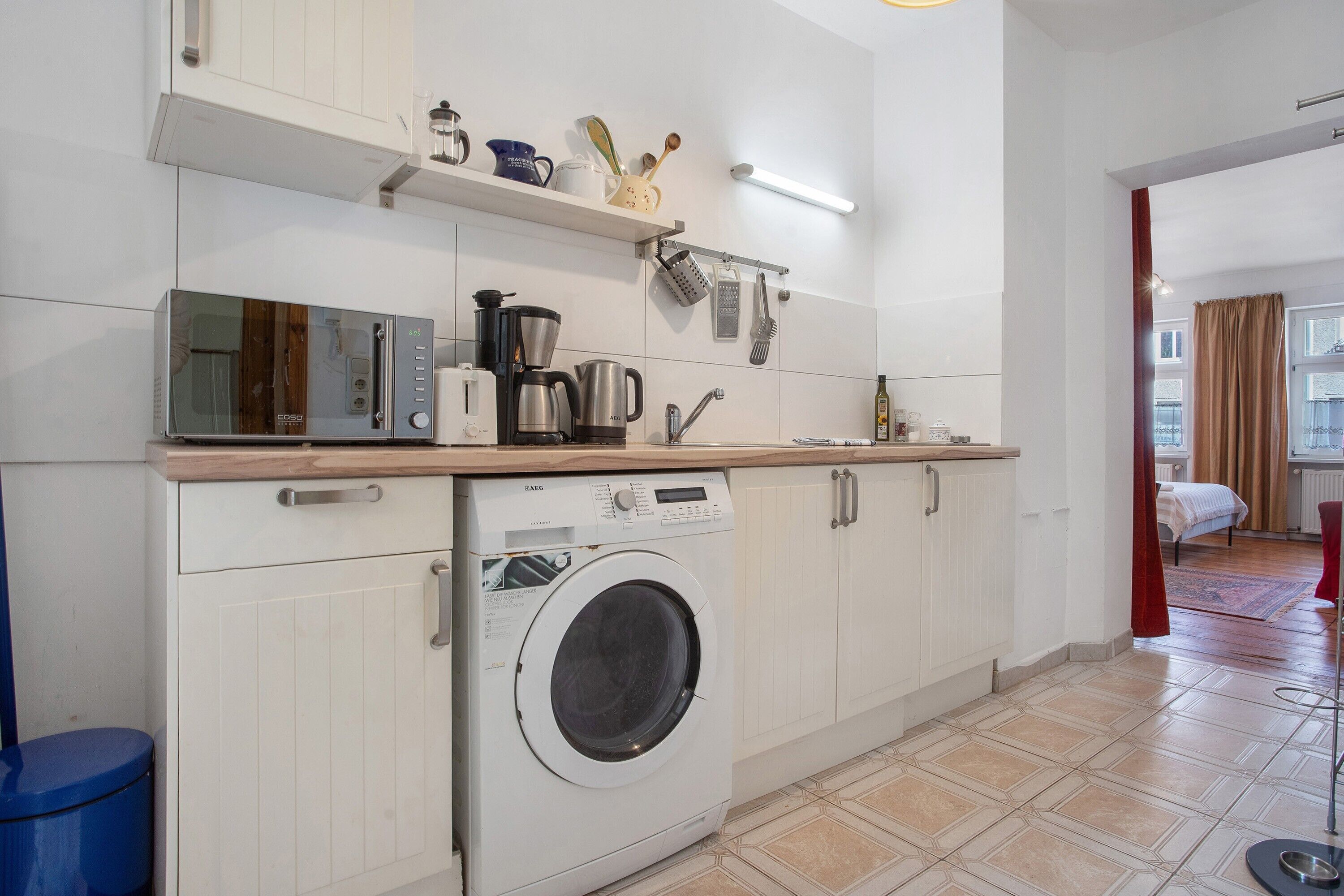 Une cuisine compacte équipée d’un lave-linge, d’un four à micro-ondes et de divers ustensiles disposés sur le plan de travail.