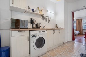 Een kleine keuken met een wasmachine, magnetron en diverse keukengerei op het aanrecht.