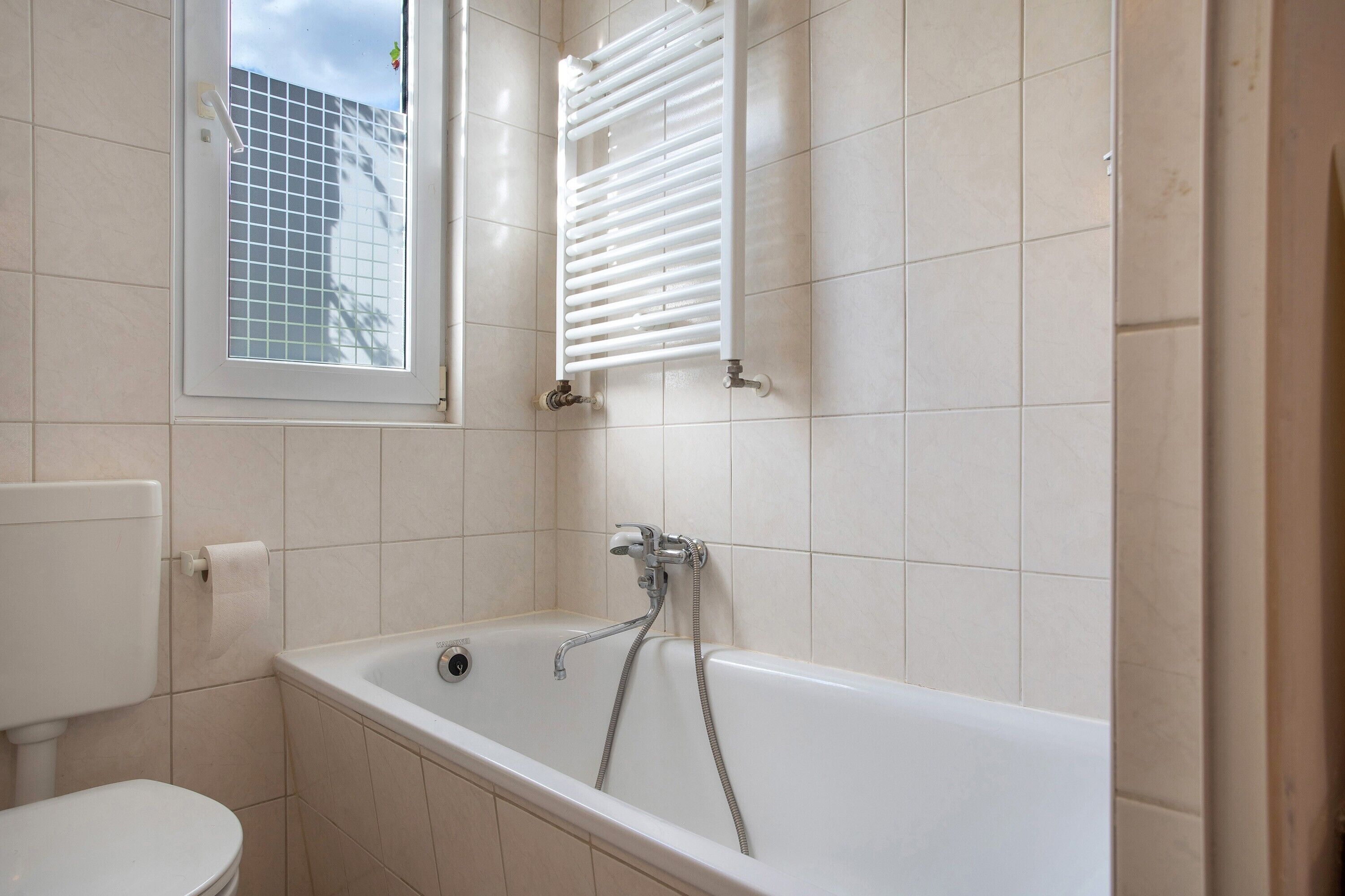 Et badeværelse med badekar, toilet og et vindue.