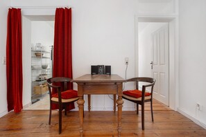 Een eetgedeelte met een houten tafel en twee stoelen, een witte deur en een plank met keukenbenodigdheden.