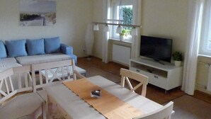 Ett vardagsrum med en soffa, ett matbord, en tv och ett fönster med gardiner.