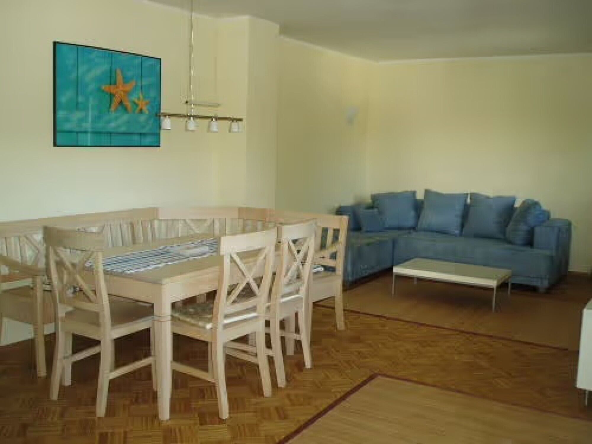 Una sala con un sofá azul, una mesa de comedor de madera y sillas.