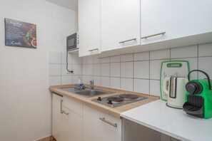 Una cocina compacta con armarios blancos, un lavamanos de acero inoxidable, un microondas y una tetera.