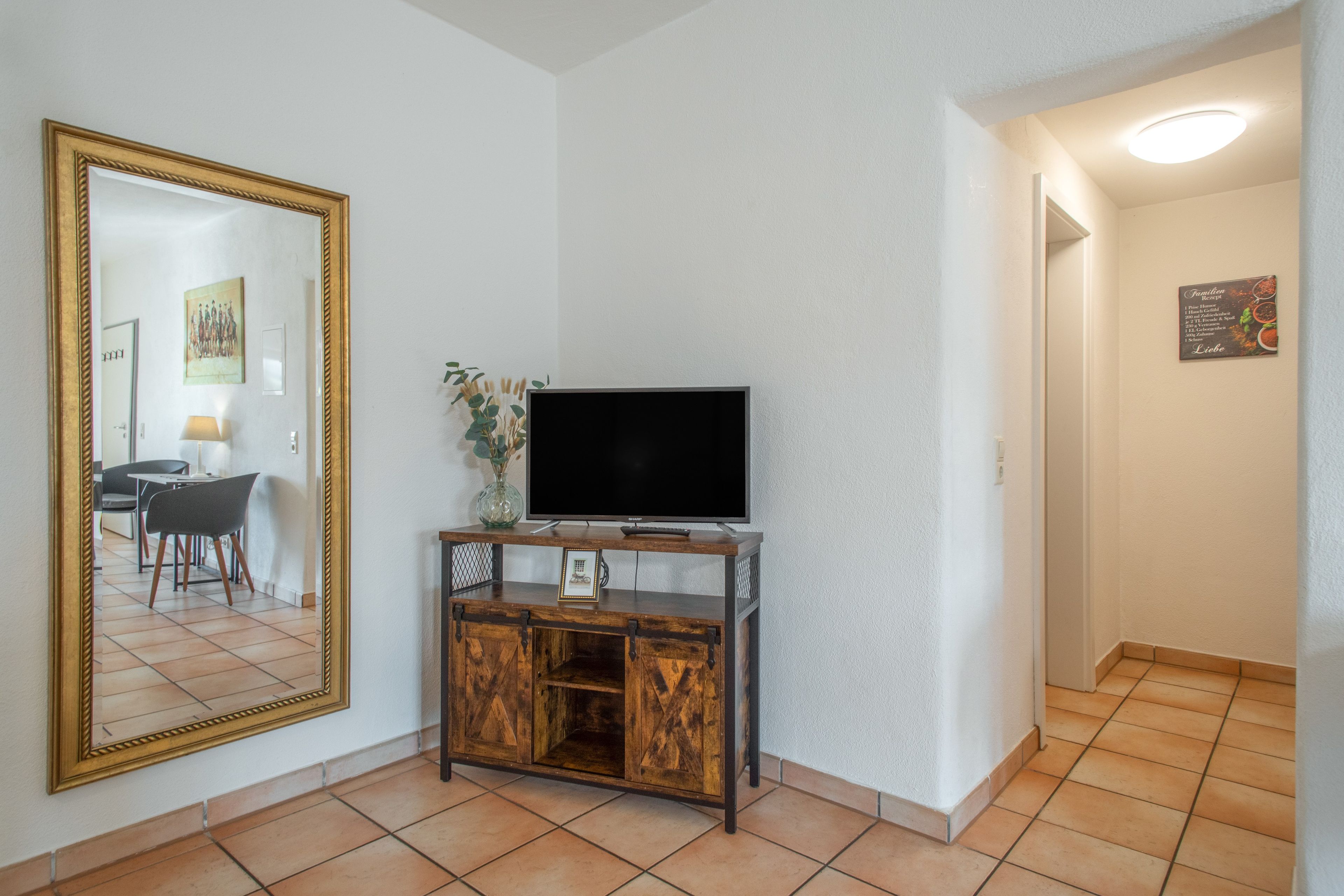 Una stanza con una televisione su un mobile in legno, un grande specchio e un quadro appeso al muro.