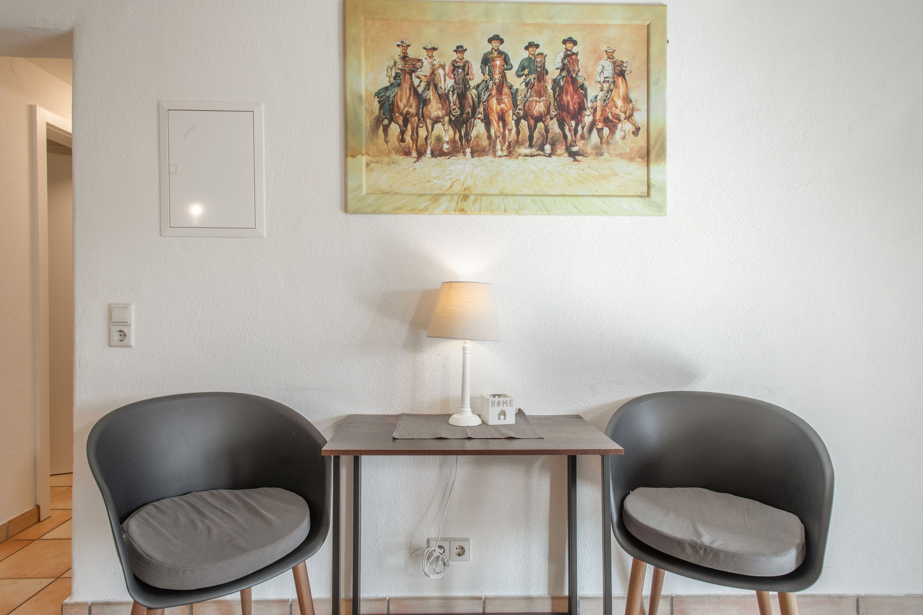 Ein Zimmer mit zwei schwarzen Stühlen, einem kleinen Tisch, einer Lampe und einem Gemälde an der Wand.