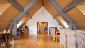 An attic bedroom with wooden beams, a dining area, and a kitchenette.