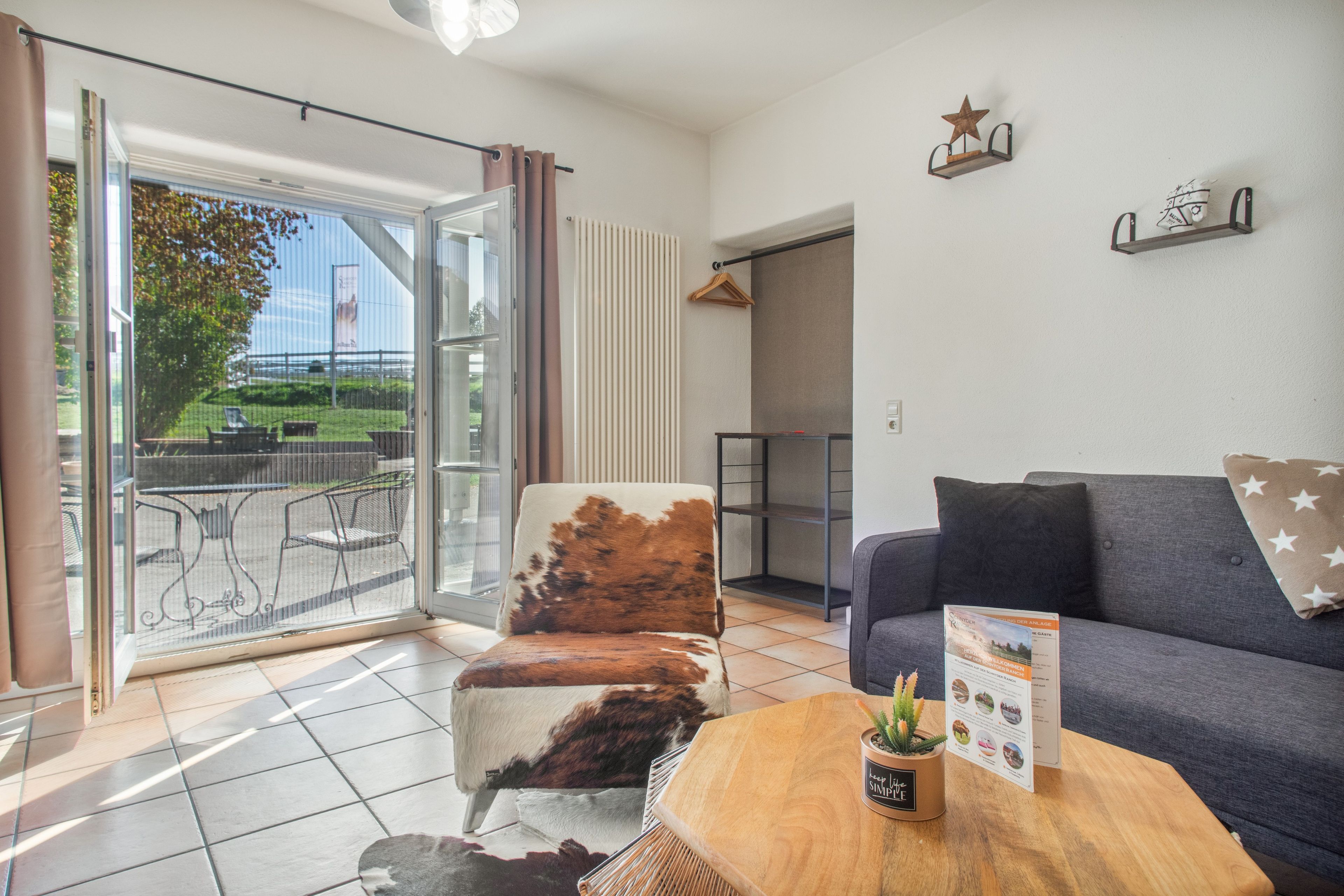 Ein Wohnzimmer mit einer Couch, einem Sessel, einem Holztisch und Blick ins Freie.