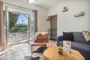 Una sala de estar con un sofá, una silla, una mesa de madera y vistas al exterior.