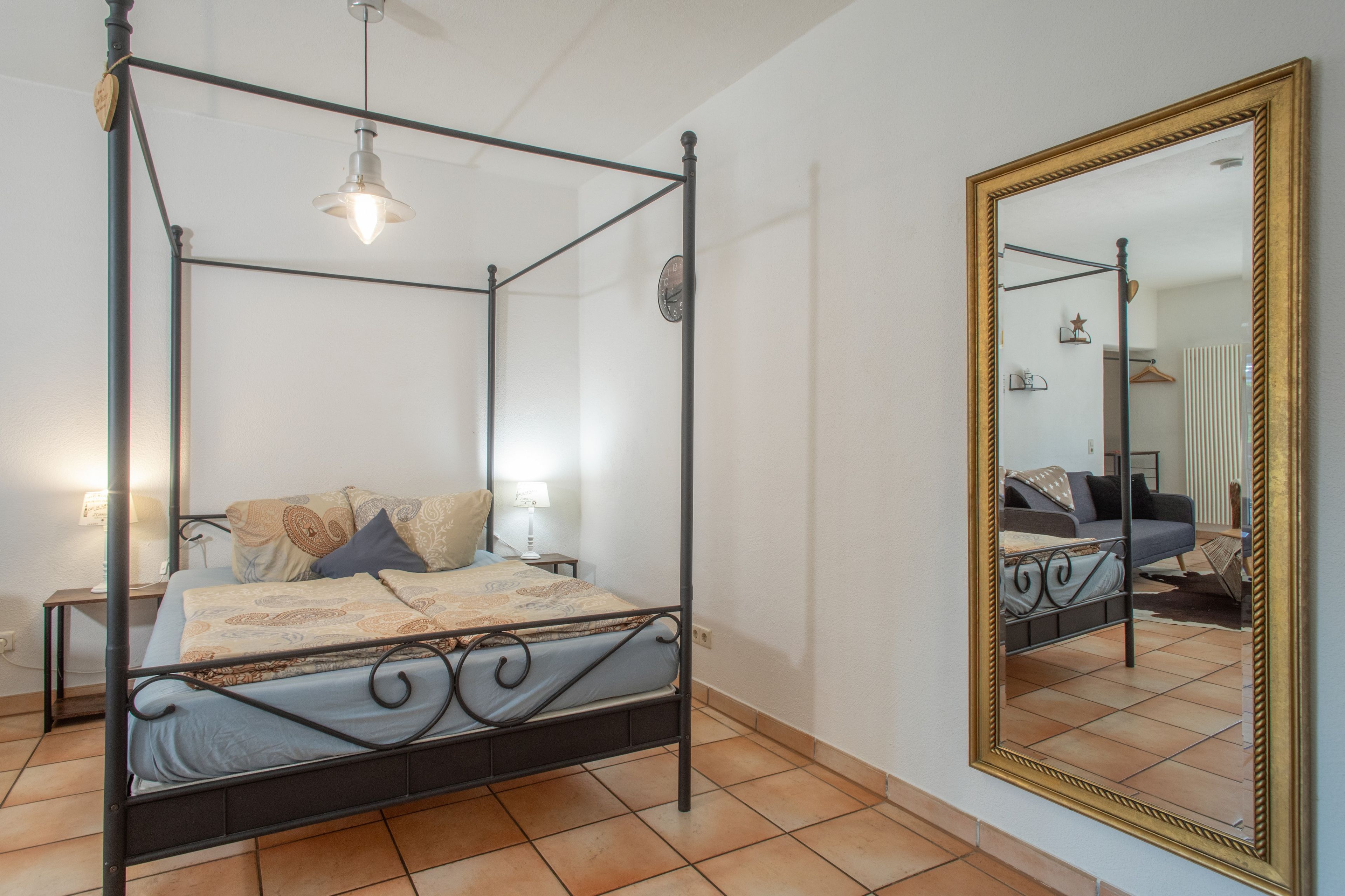 Ein Bett mit Himmelbett, ein Nachttisch mit Lampe und ein großer Spiegel an der Wand.