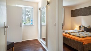 Un dormitorio con cama, ventana, puerta y una lámpara fijada a la pared.