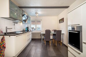 Une cuisine moderne avec des meubles blancs, un plan de travail noir, un four Bosch et un coin repas comprenant une table et des chaises.