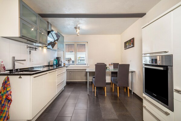 A modern kitchen with white cabinets, a black countertop, a Bosch oven, and a dining area with a table and chairs.