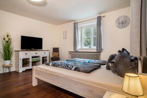 Une chambre à coucher avec un lit, une télévision, une fenêtre avec des rideaux, un radiateur et une plante en pot.