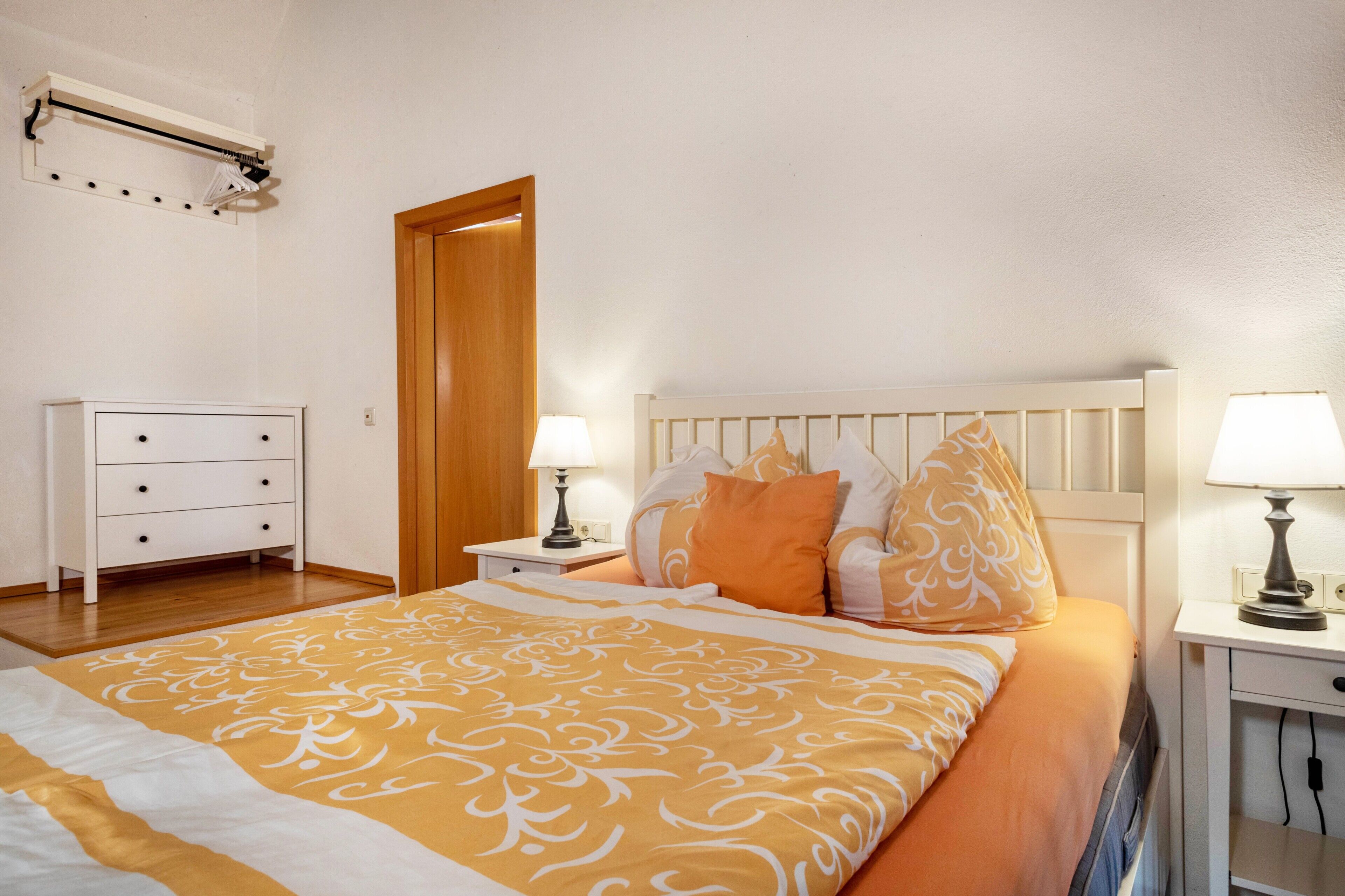 Un dormitorio con cama, mesitas de noche, cómoda y una puerta.