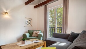 Una sala de estar con un sofá, una mesa de centro, una planta pequeña y una ventana con cortinas.