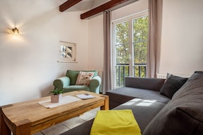 A living room with a sofa, a coffee table, a small plant, and a window with curtains. - Apartment 'Maisonette' with Shared Garden and Wi-Fi (Ravensburg)