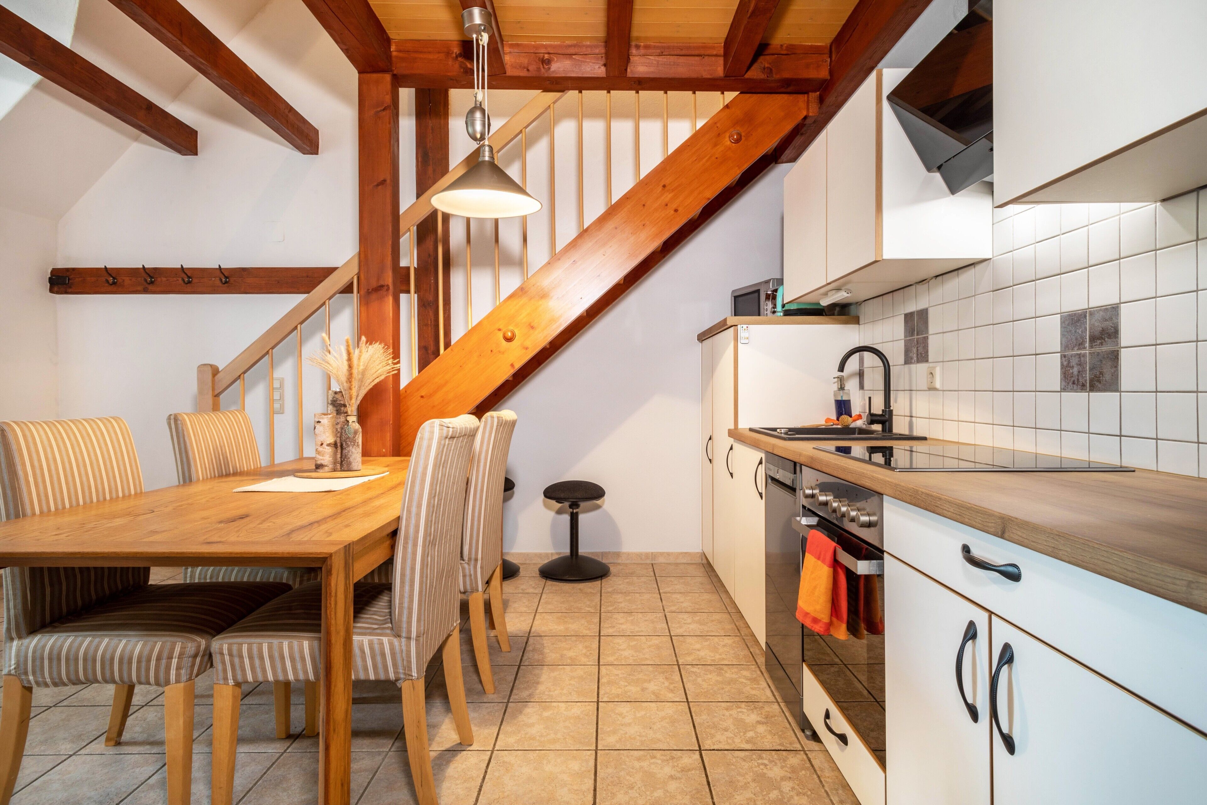 Una cocina con vigas de madera, una mesa de comedor con sillas, una mesita redonda y un salpicadero de azulejos.