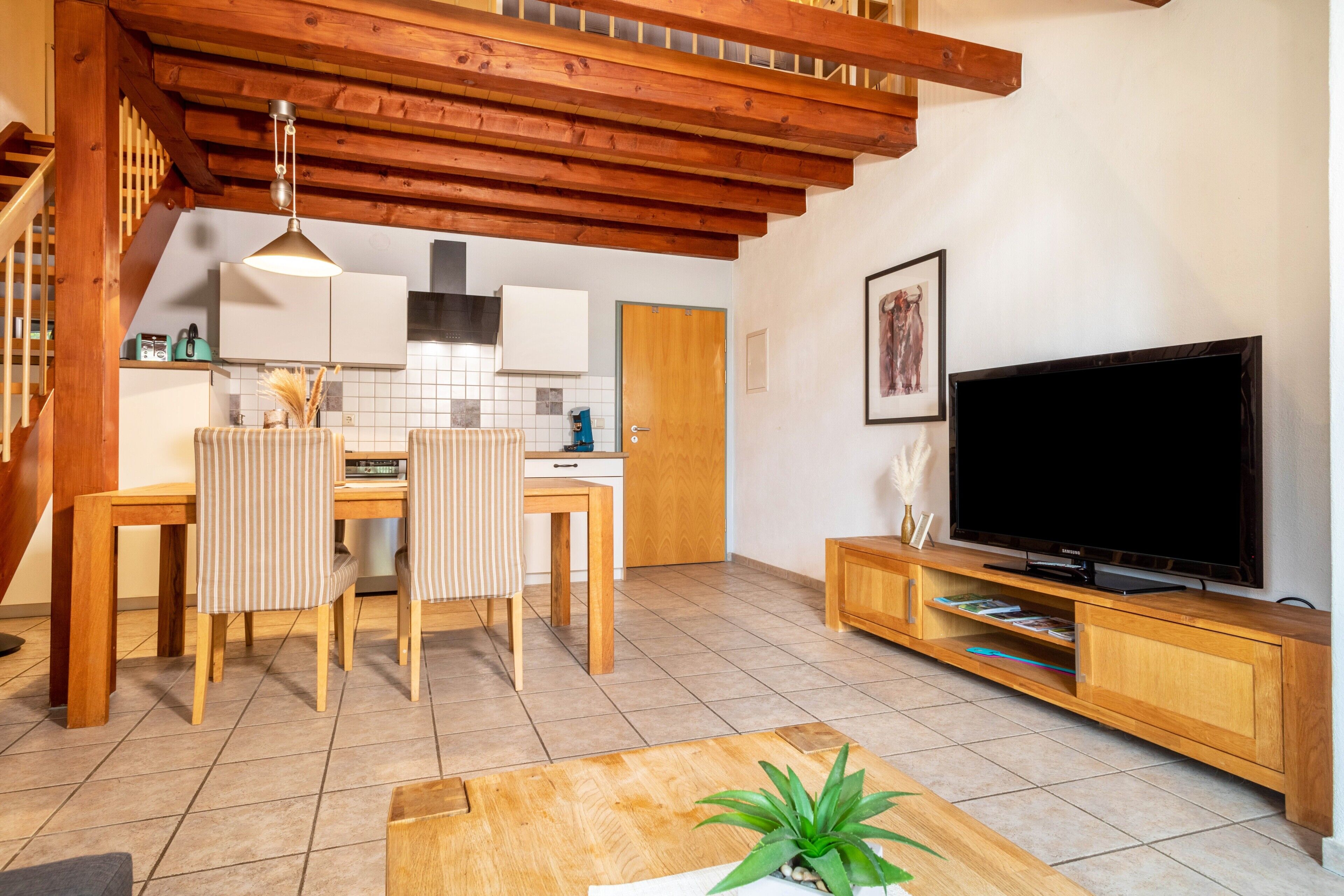 Ein modernes Wohnzimmer mit einem Holzesstisch, Stühlen, einem Fernseher und einer Treppe.