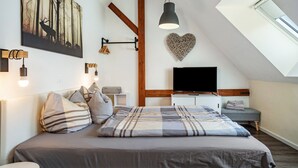 A bedroom with a bed, a TV, a heart-shaped wall decoration, a skylight, and a painting of deer. - Room 2, cozy, bright double room with sloping ceiling (Ravensburg)