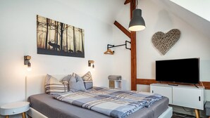 Quarto com cama, mesas de cabeceira, televisão, luminária fixada na parede, decoração em formato de coração e pintura com tema de floresta.
