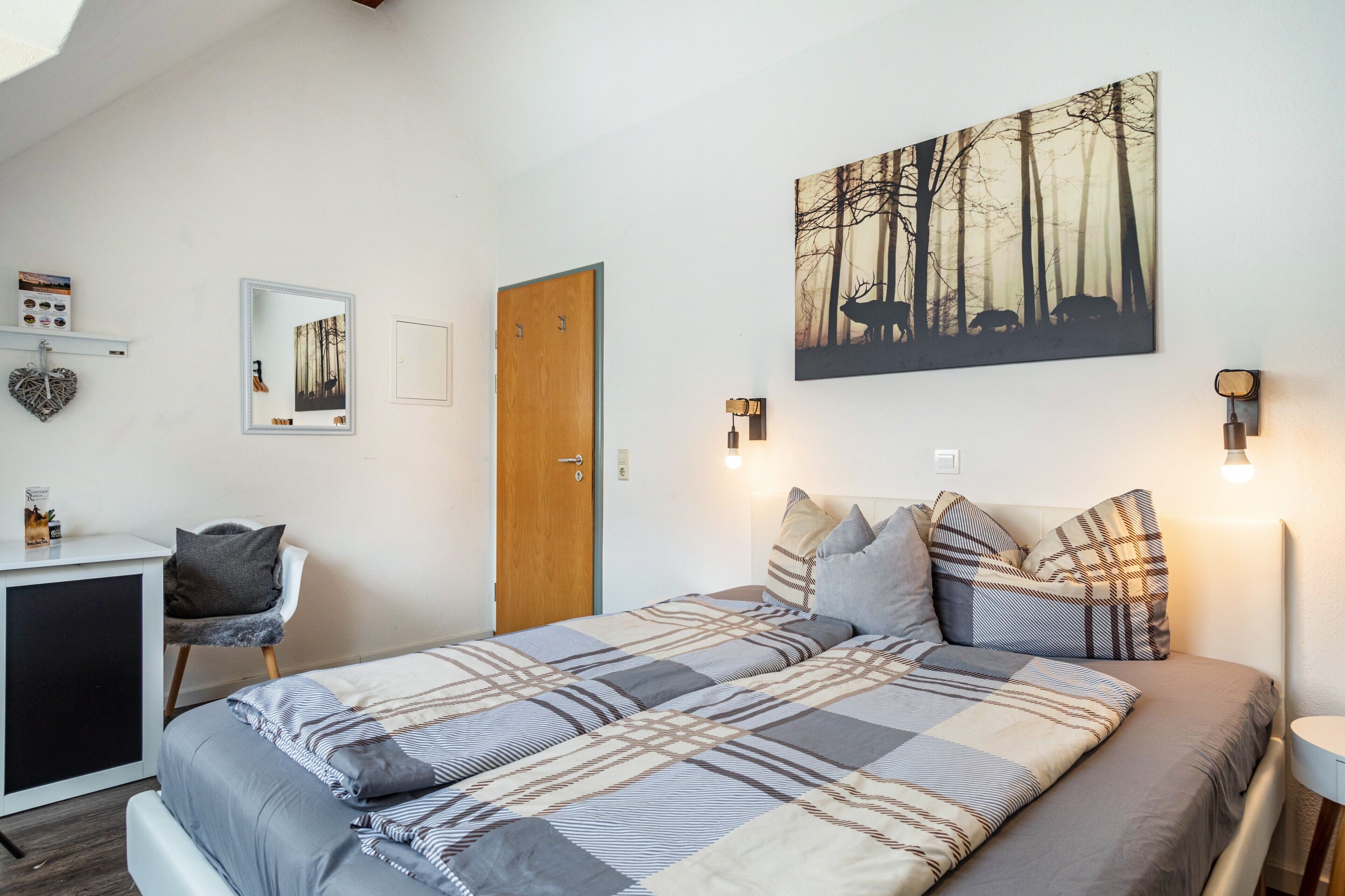 A bedroom with a bed, a desk, a chair, a door, and wall-mounted lights.